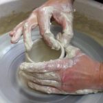 Hände formen ein Gefäß aus Ton an der Töpferscheibe