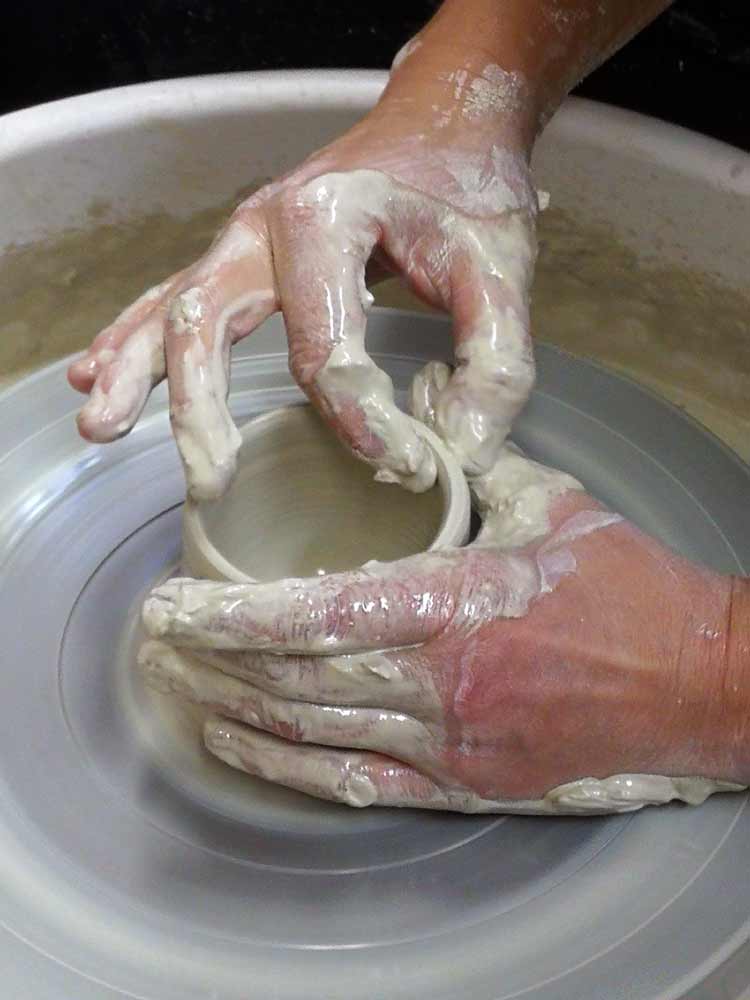 Hände formen ein Gefäß aus Ton an der Töpferscheibe