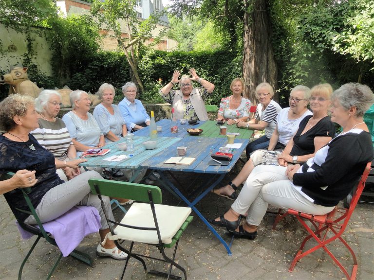 ältere Damen und Herren sitzen um ein Tisch herum im Hof des Haus Steinstrasse