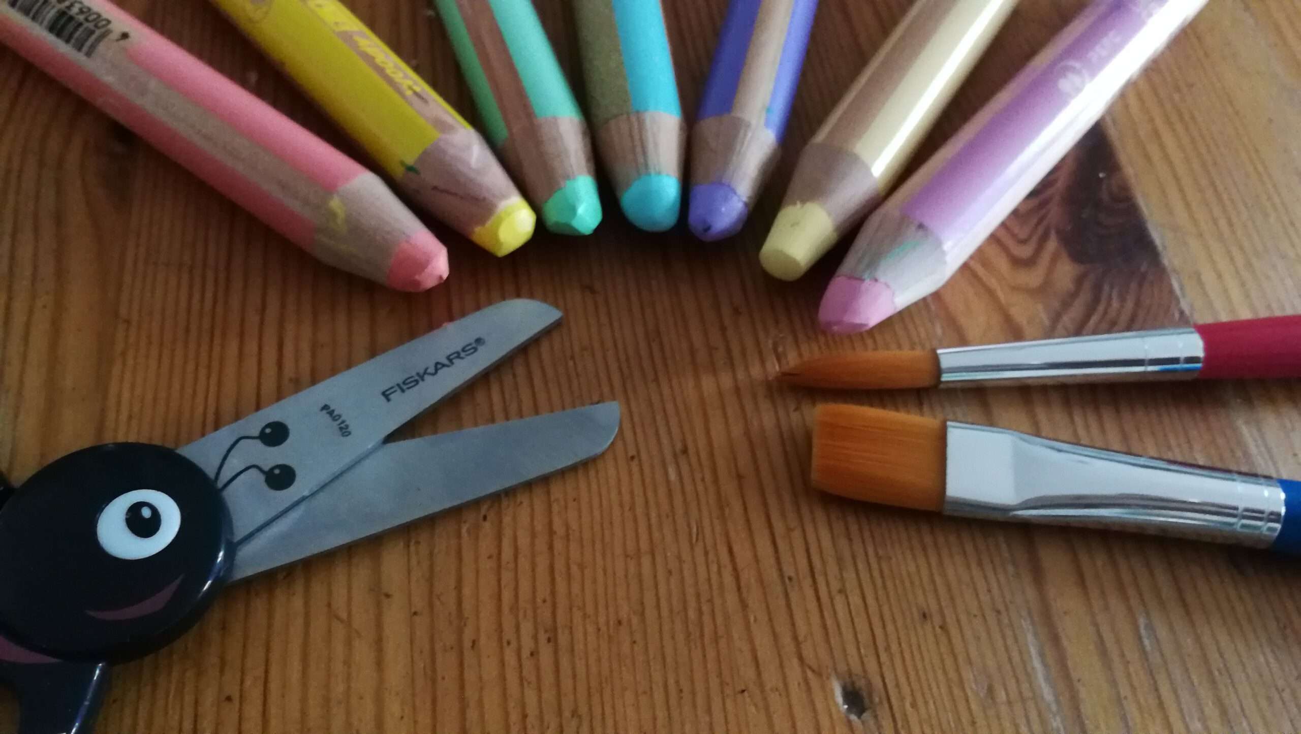 Im Halbkreis gelegt: Schere, Sieben bunte Stifte, zwei Pnsel