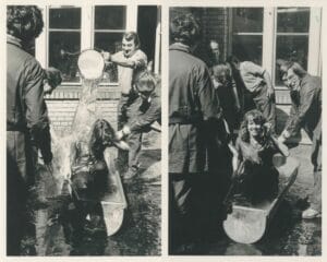 Zu sehen sind zwei Schwarz-Weiß-Fotos, auf denen eine Auszubildende in einem Wasserbottich sitzt, auf dem linken Bild wird ein Eimer Wasser über ihr ausgeschüttet, auf dem rechten Bild sieht sie in die Kamera.