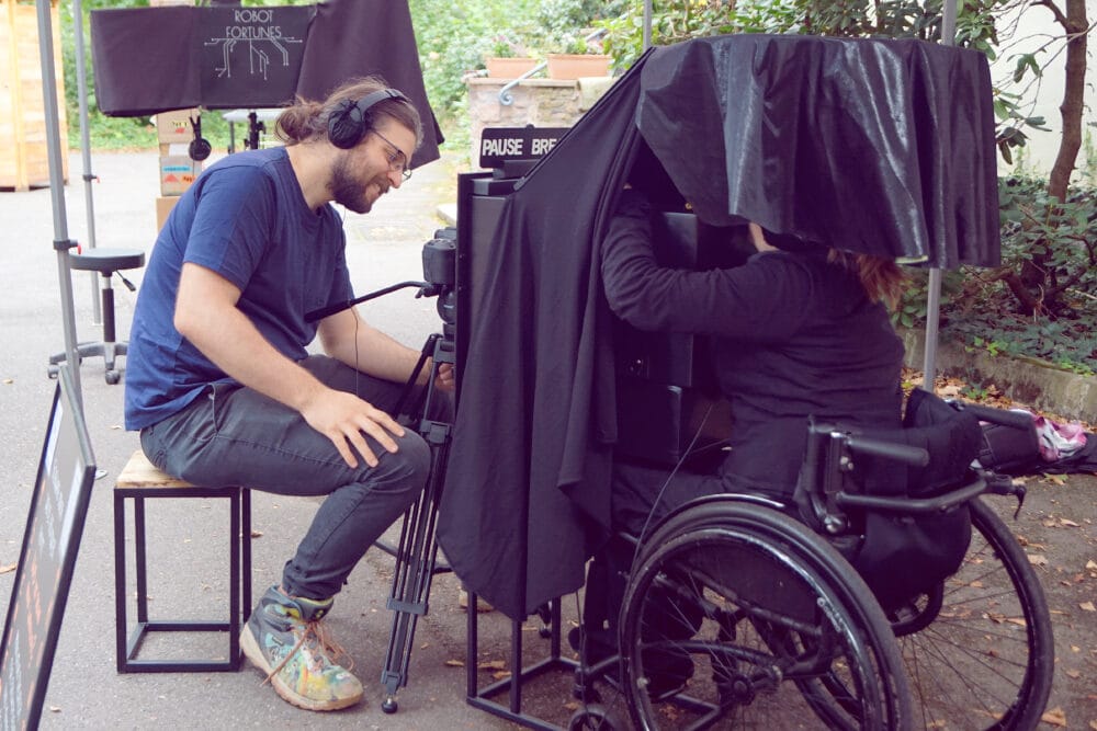 Eine Puppenspielerin spielt in einem Kasten für einen Zuschauer ein kleines Theaterstück. Die Bühne ist so ausgelegt, dass immer nur eine Person das Stück sehen kann. Der Zuschauer muss sich dafür auf einen Stuhl setzen und das Theaterstück in einem kleinen Schaukasten verfolgen.