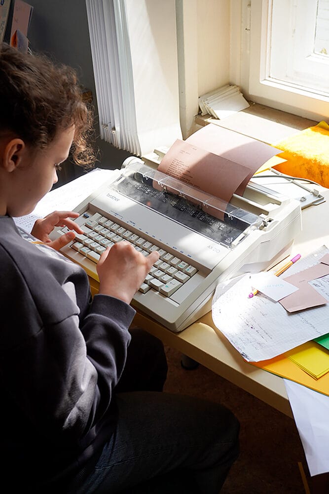Ein Kind schreibt an einer Schreibmaschine Beschreibungstexte für Bilder in einer AUsstellung.
